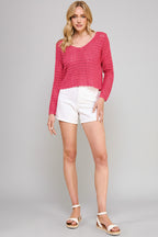 Woman wearing a hot pink crochet top and white shorts on a beige background