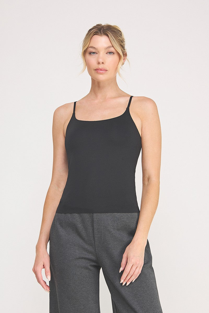 A woman modeling a black cami bralette  paired with dark gray pants against a light gray studio background.