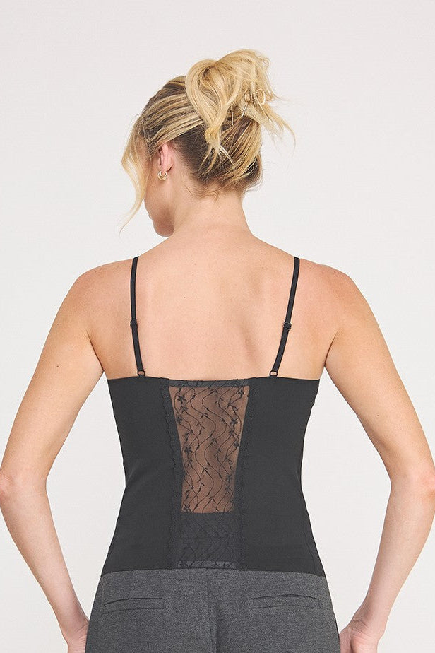 Back view of a  woman modeling a black cami bralette with black lace insert  paired with dark gray pants against a light gray studio background.