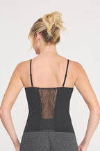 Back view of a  woman modeling a black cami bralette with black lace insert  paired with dark gray pants against a light gray studio background.