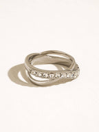 A silver-toned double-band ring with a row of clear round-cut stones on the front band, photographed on a clean off-white background with a soft shadow.