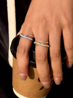 Hand with a silver-toned and gold toned double-band ring with a row of clear round-cut stones on the front band, 