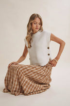 Woman wearing a creame sleeveless sweater and brown plaid skirt on a plain background