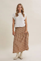 Woman wearing a cream sleeveless sweater, plaid skirt, on a plain background