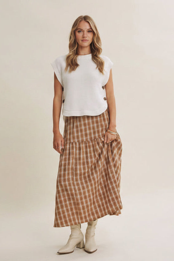 Woman wearing a cream sleeveless sweater, plaid skirt, on a plain background