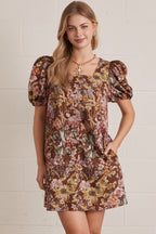 Woman wearing a floral dress with puff sleeves against a white brick wall.