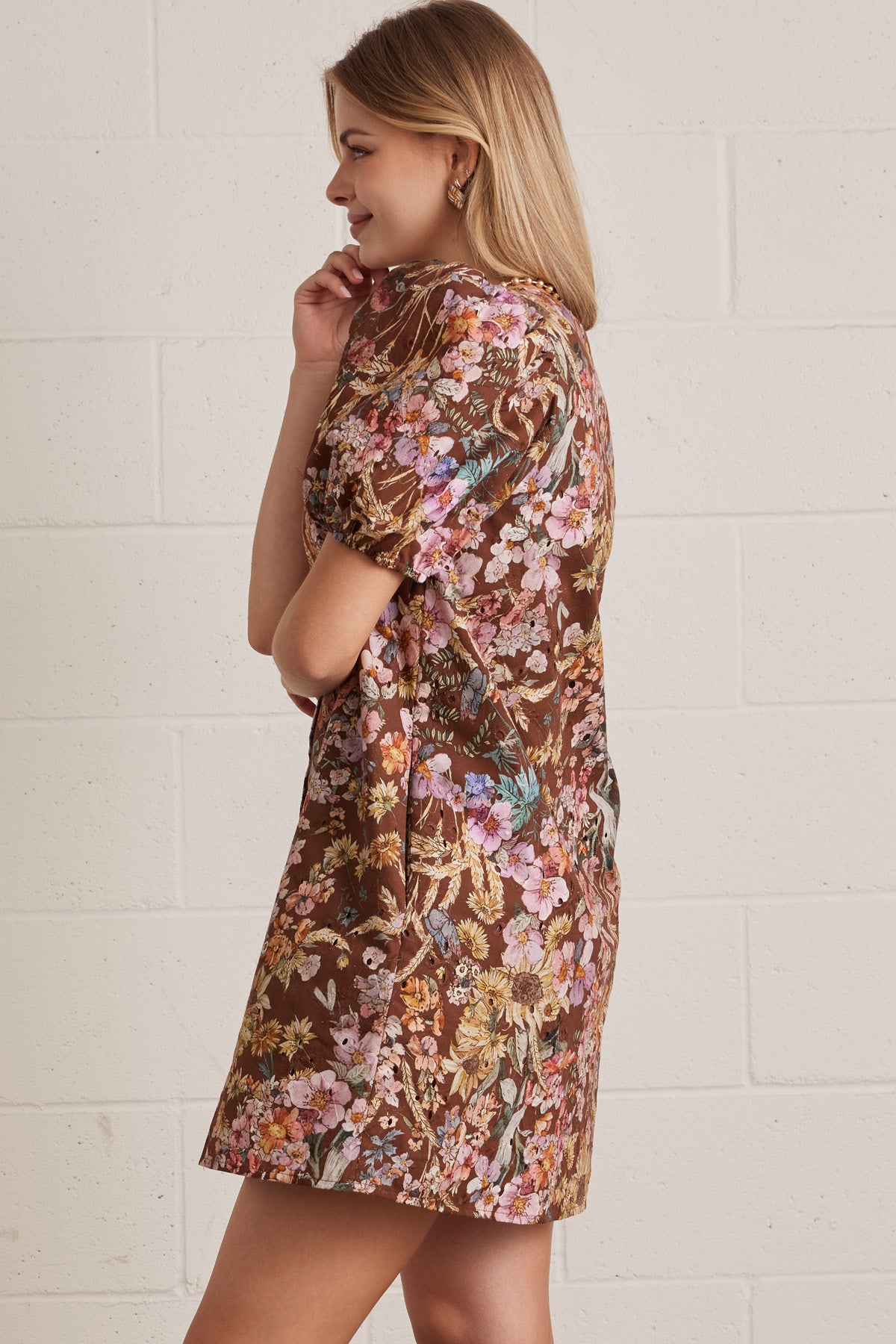 Woman wearing a floral dress with puff sleeves against a white brick wall.