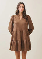 Woman wearing a mocha tiered dress against a plain background