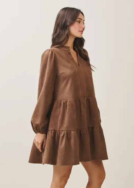 Woman wearing a mocha tiered dress against a plain background