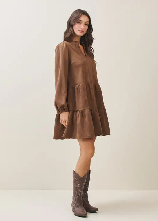 Woman wearing a mocha tiered dress and matching boots against a plain background