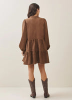 Back view of a woman wearing a mocha tiered dress and matching boots against a plain background