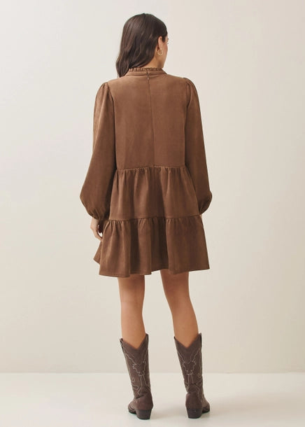 Back view of a woman wearing a mocha tiered dress and matching boots against a plain background