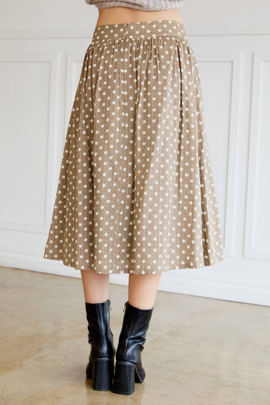 Woman wearing a tan polka dot skirt with cream dots and black boots indoors.