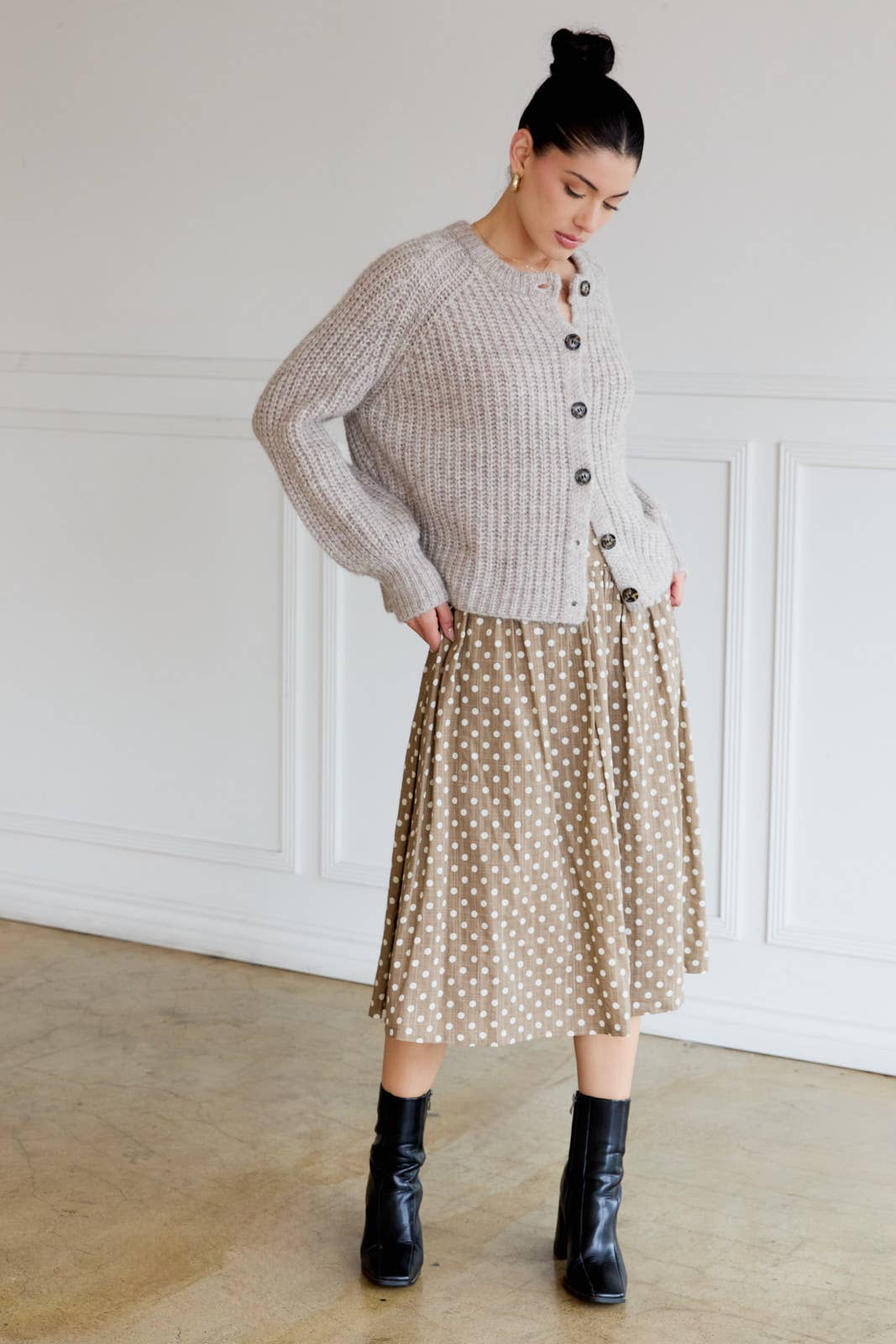 Woman wearing tan polka dot skirt with cream dots against a white paneled wall.