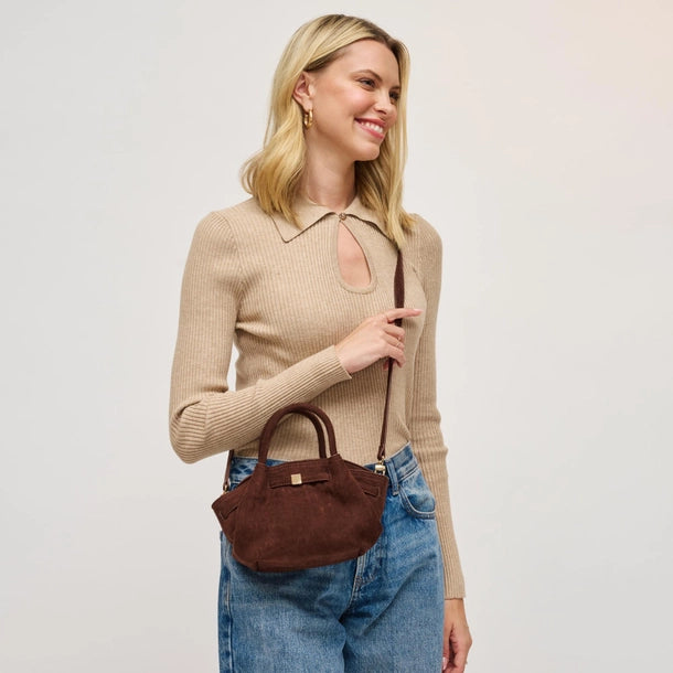 Woman holding chocolate handbag wearing blue jeans on a plain background