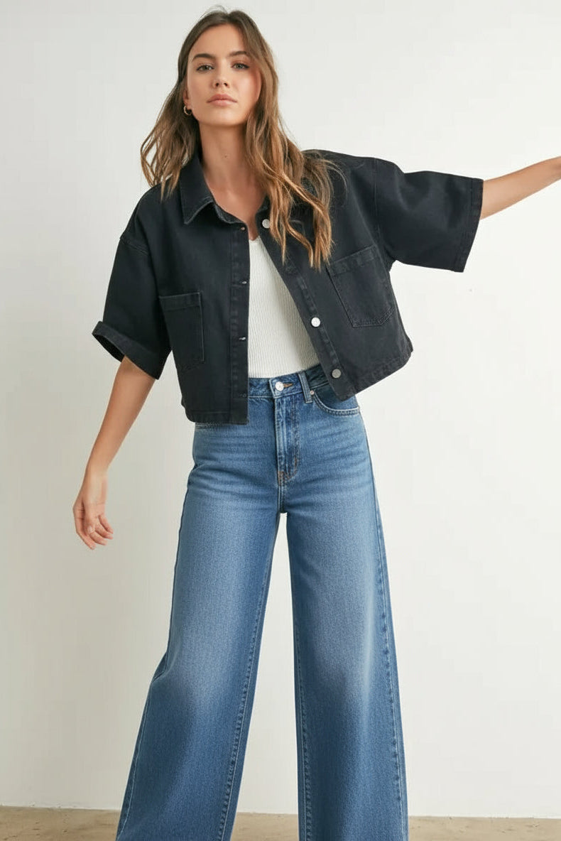 Woman wearing a black denim cropped top, white shirt, and checkered shorts against a plain background