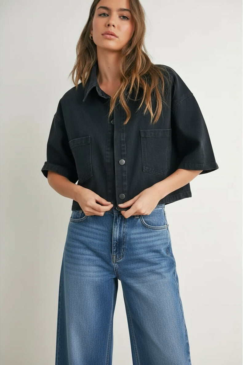 Woman wearing a black denim cropped denim top and black and white checkered shorts on a plain background
