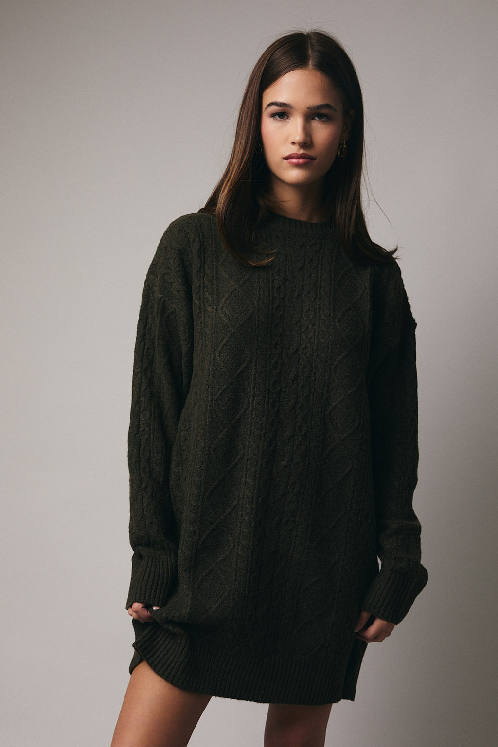 Woman wearing an olive cable knit sweater dress against a gray background