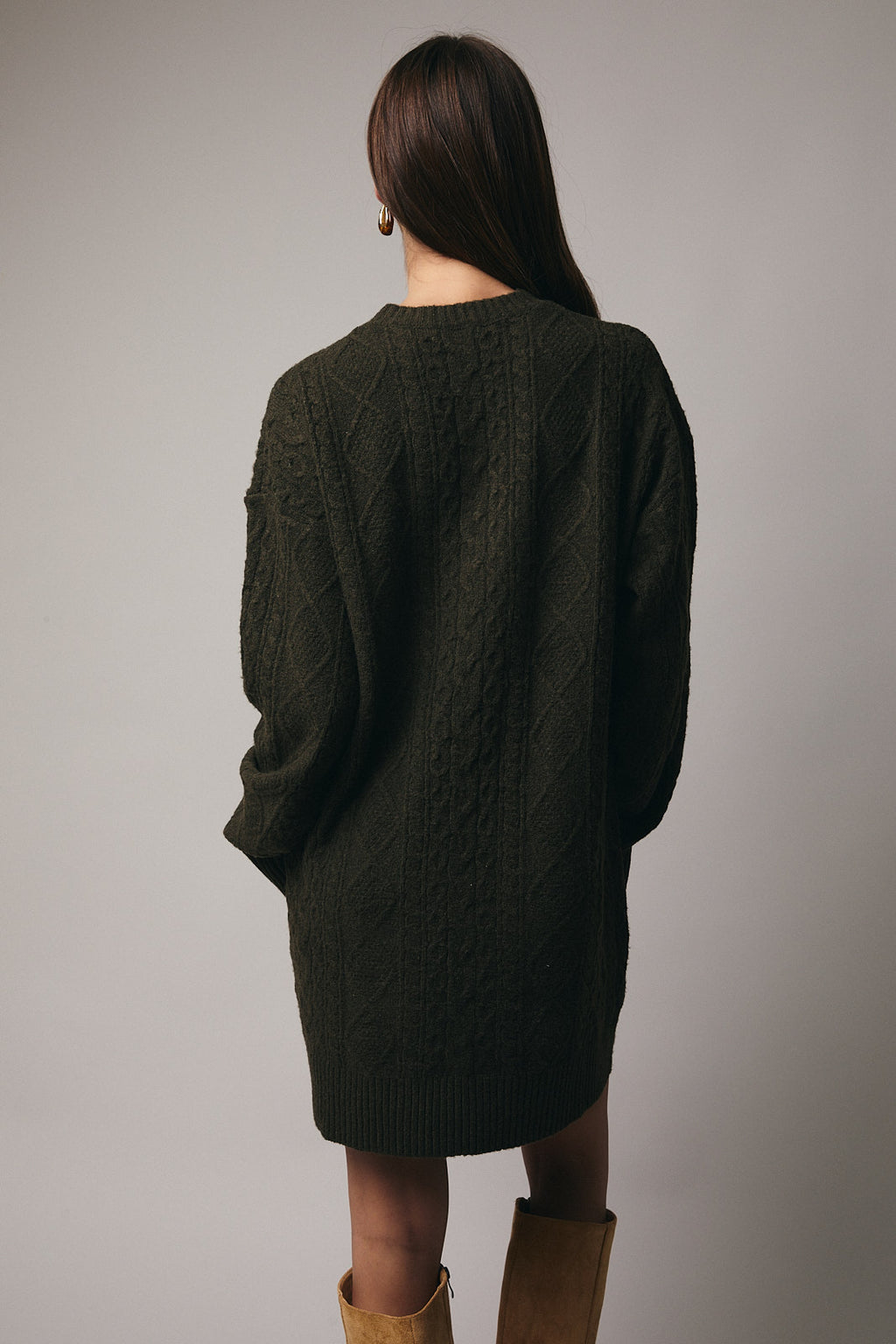 Back view of a woman wearing an olive cable knit sweater dress against a gray background