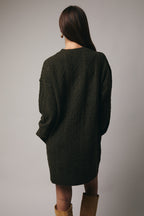 Back view of a woman wearing an olive cable knit sweater dress against a gray background