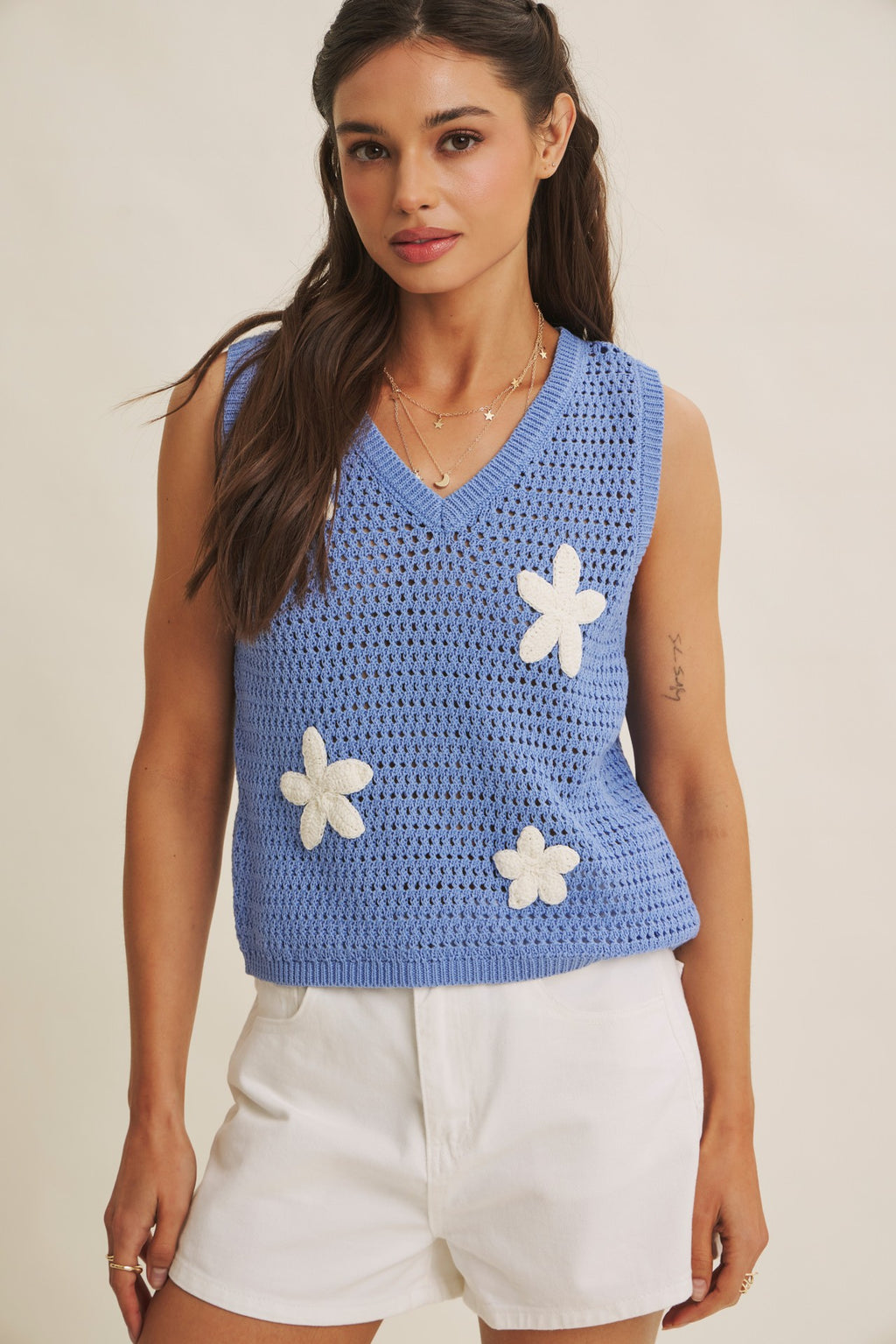 Woman wearing a blue knit top with white flower appliques on a beige background