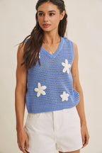 Woman wearing a blue knit top with white flower appliques on a beige background