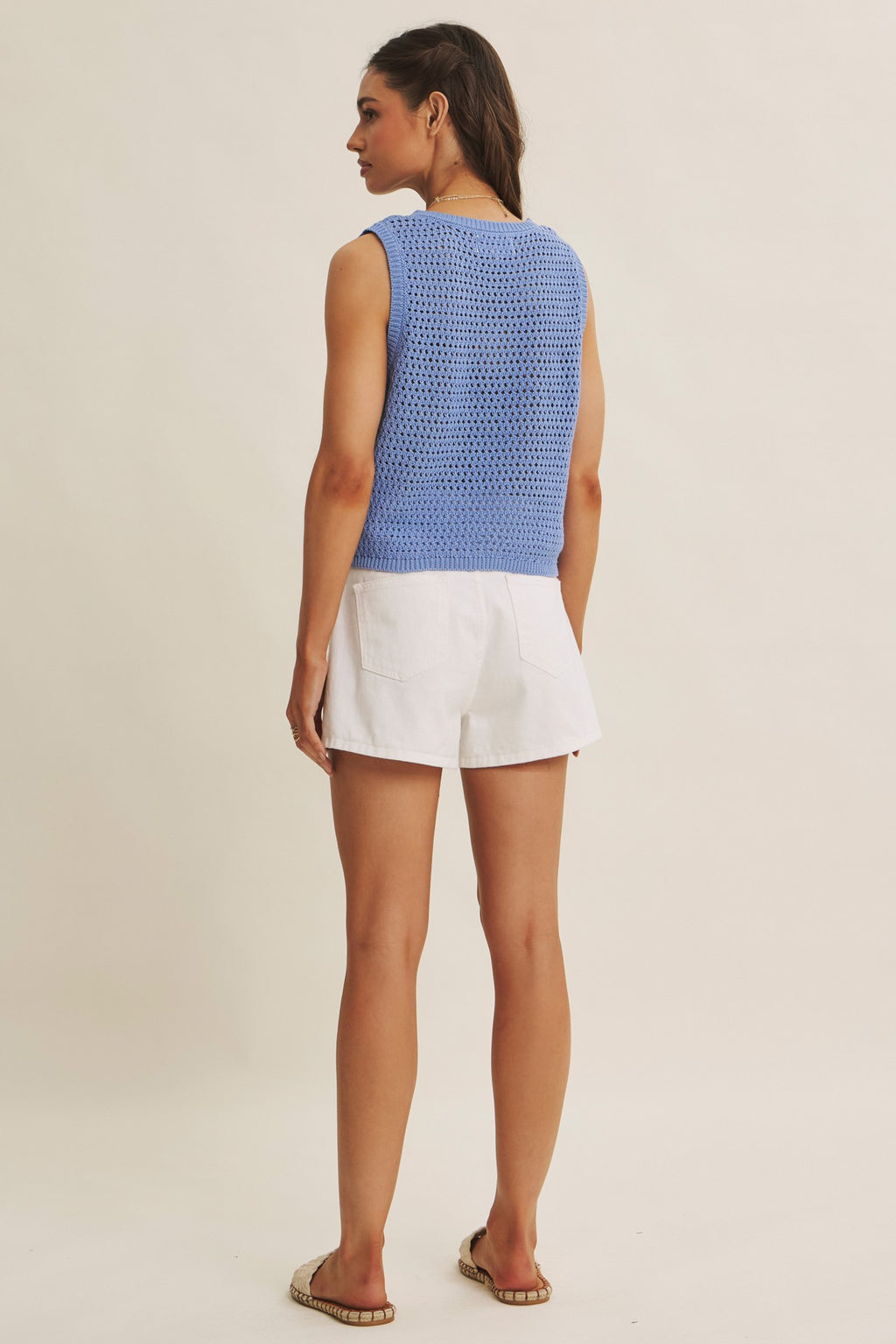 Back view of woman wearing a blue knit top with white flower appliques on a beige background