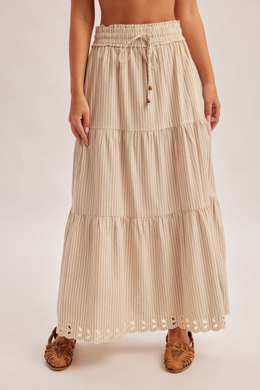 Woman wearing a natural tiered striped skirt with embroidered cutout on a plain background