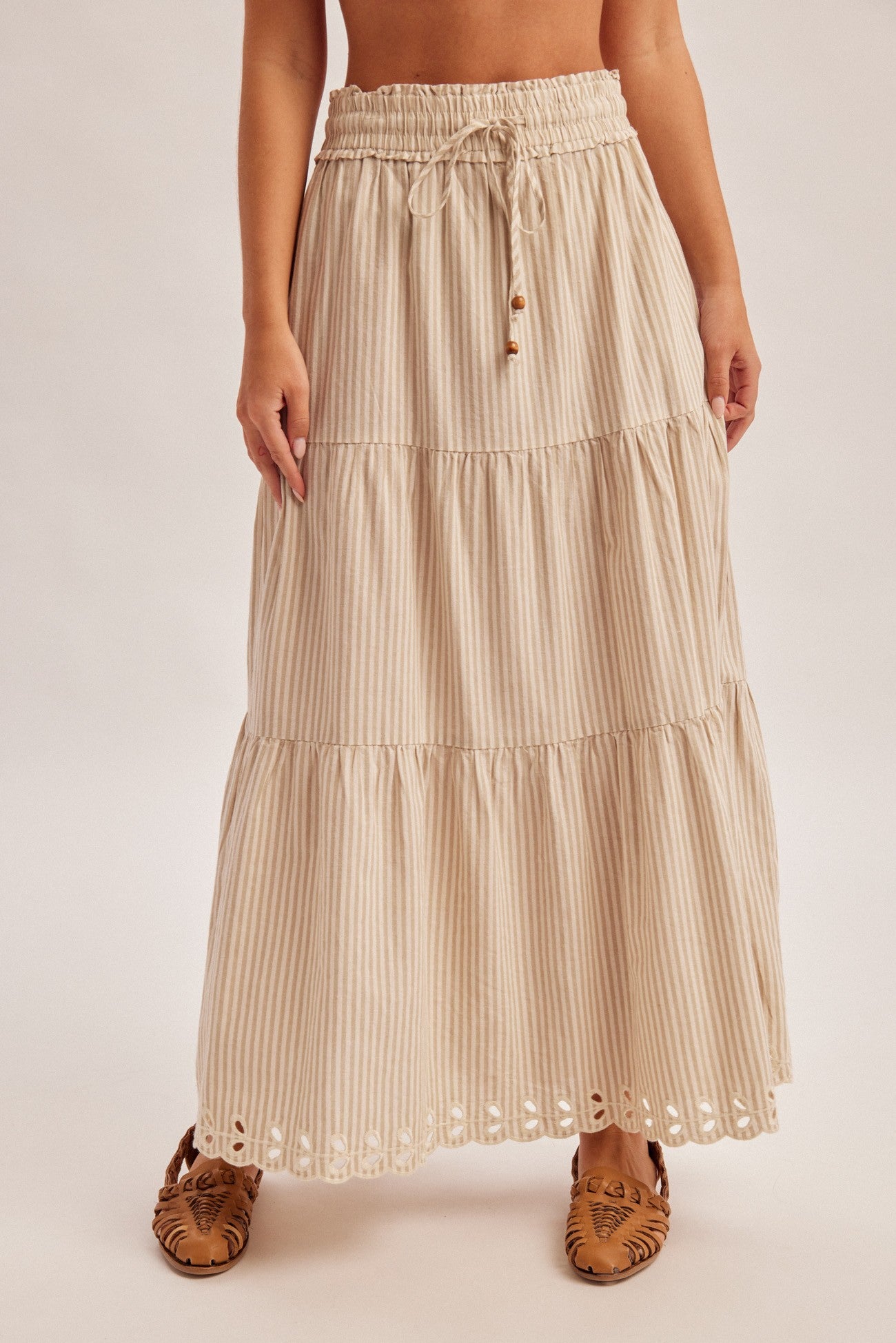 Woman wearing a natural tiered striped skirt with embroidered cutout on a plain background