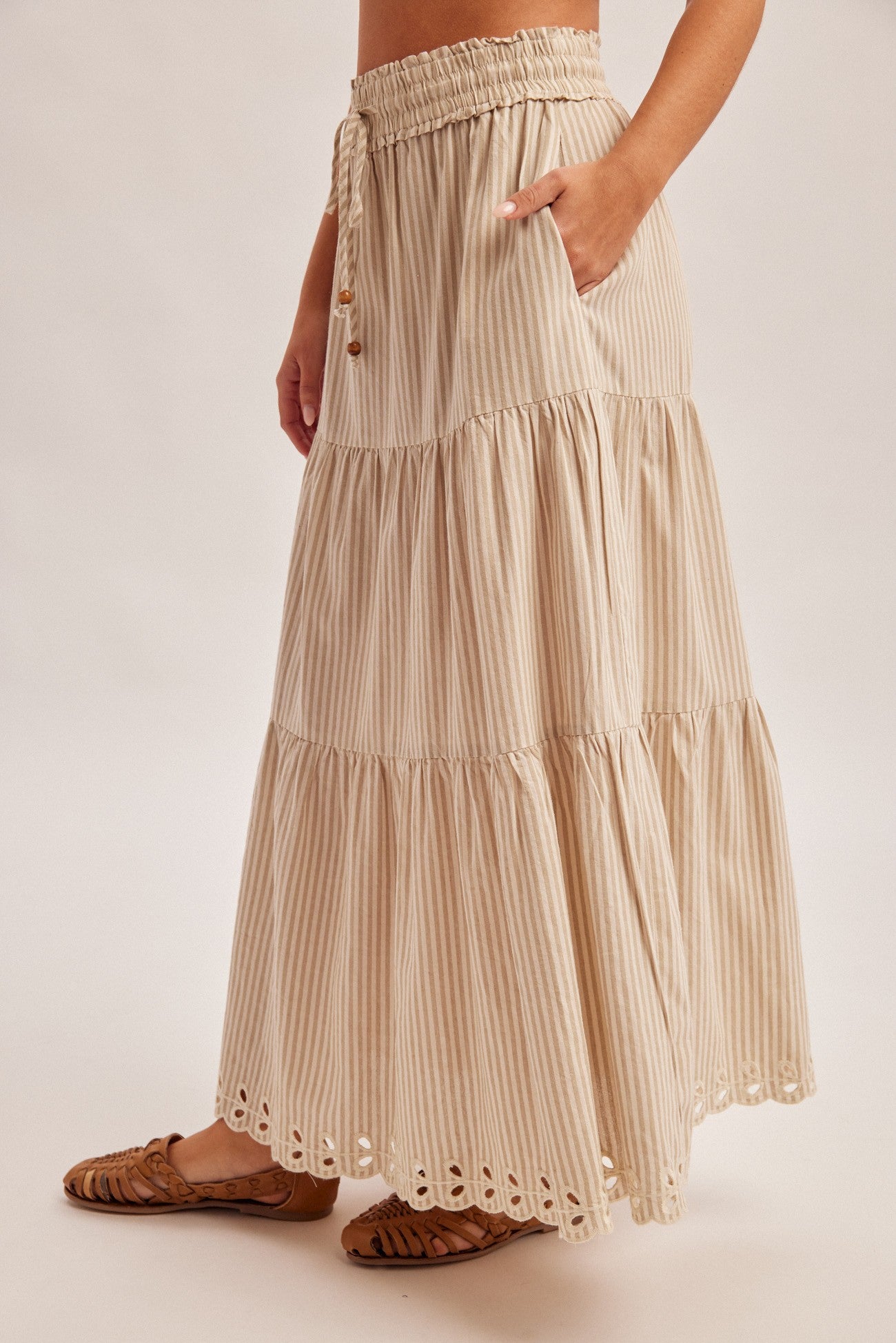 Woman wearing a natural tiered striped skirt with embroidered cutout on a plain background