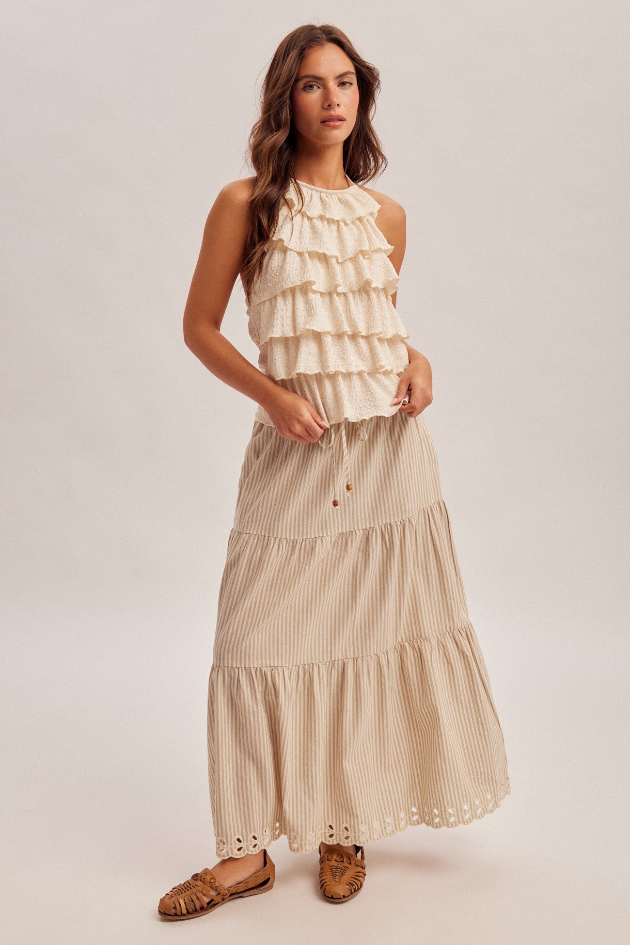 Woman wearing a natural tiered striped skirt with ruffled top on a plain background