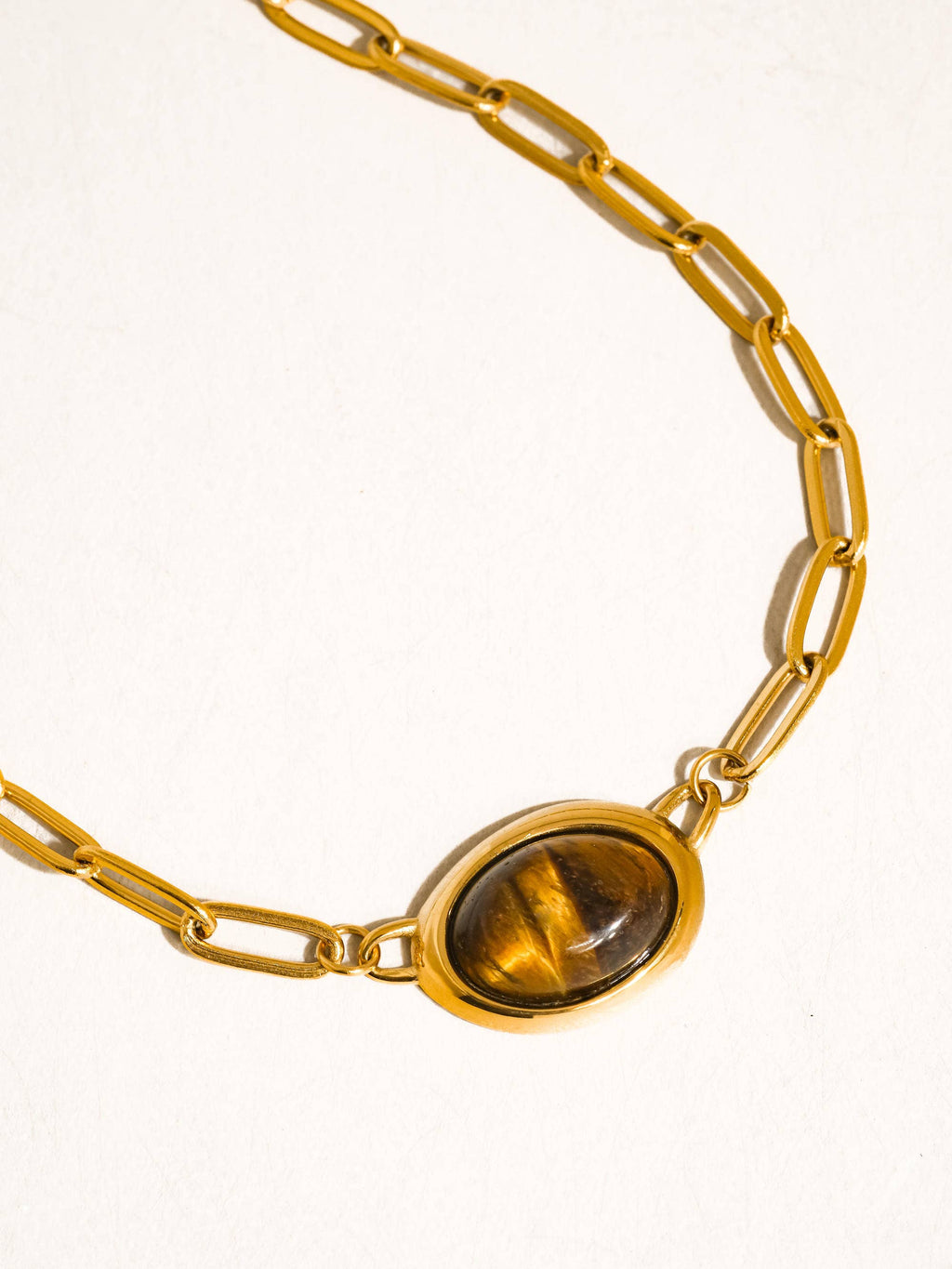 Gold plated paper clip chain necklace with a cat's eye stone on a white background