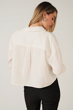 Back view of a woman modeling a white long-sleeve shirt, paired with black pinstriped pants, against a solid beige background.