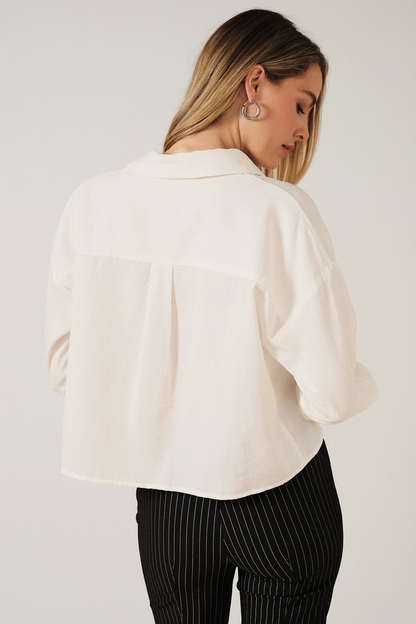  Back view of a woman modeling a white long-sleeve shirt, paired with black pinstriped pants, against a solid beige background.