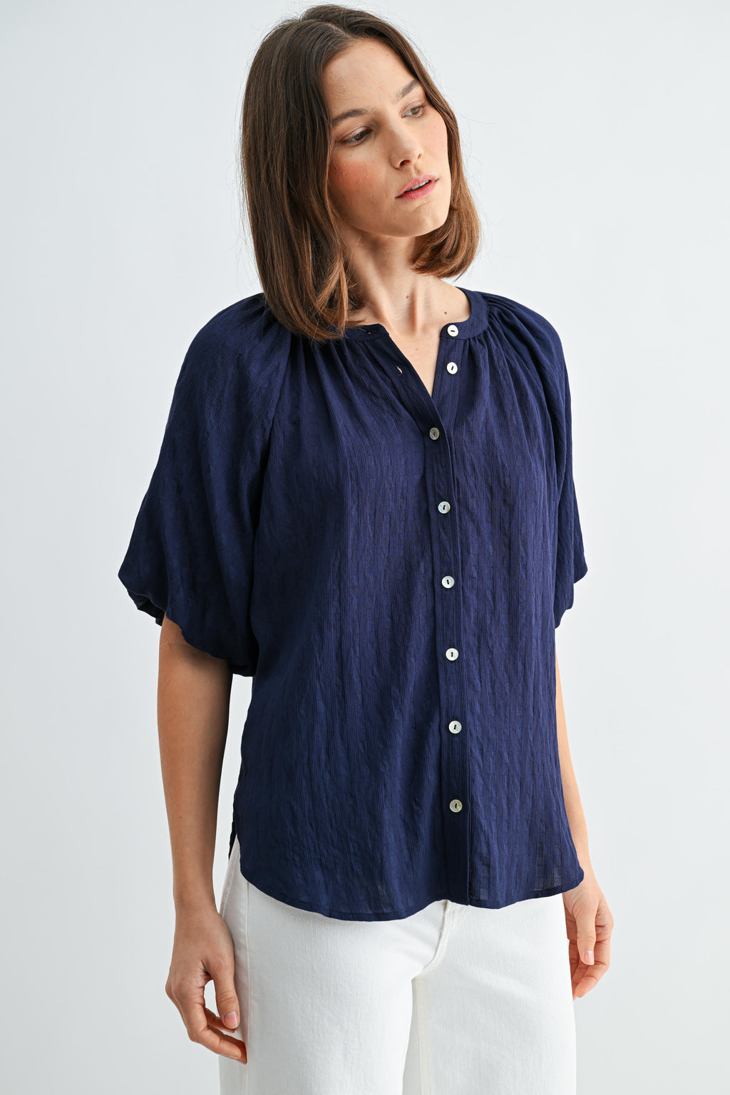 Woman wearing a textured navy blue blouse with short balloon sleeves with white buttons on a light gray background