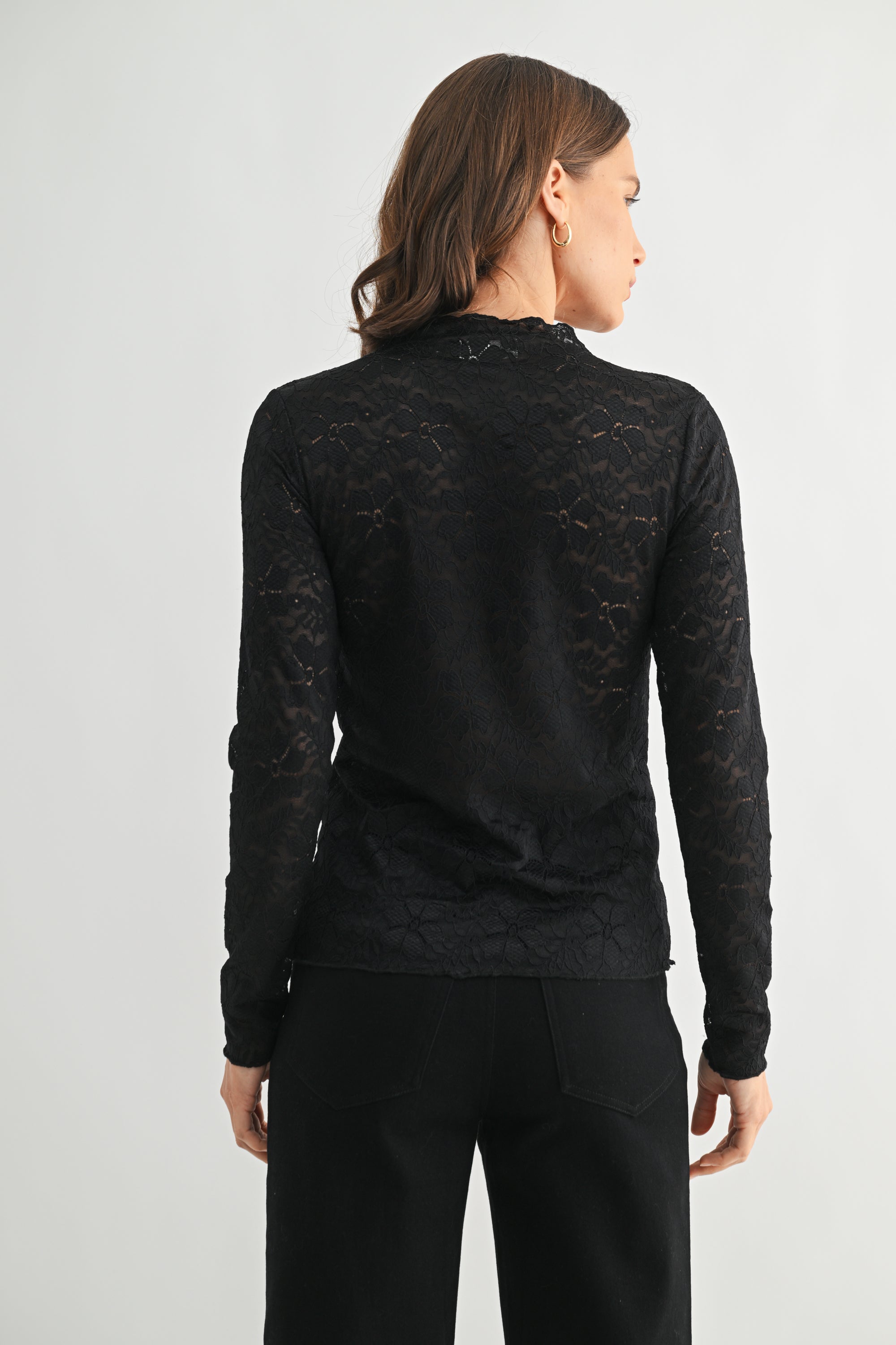 Back view of woman wearing a black lace long-sleeve top on a light gray background