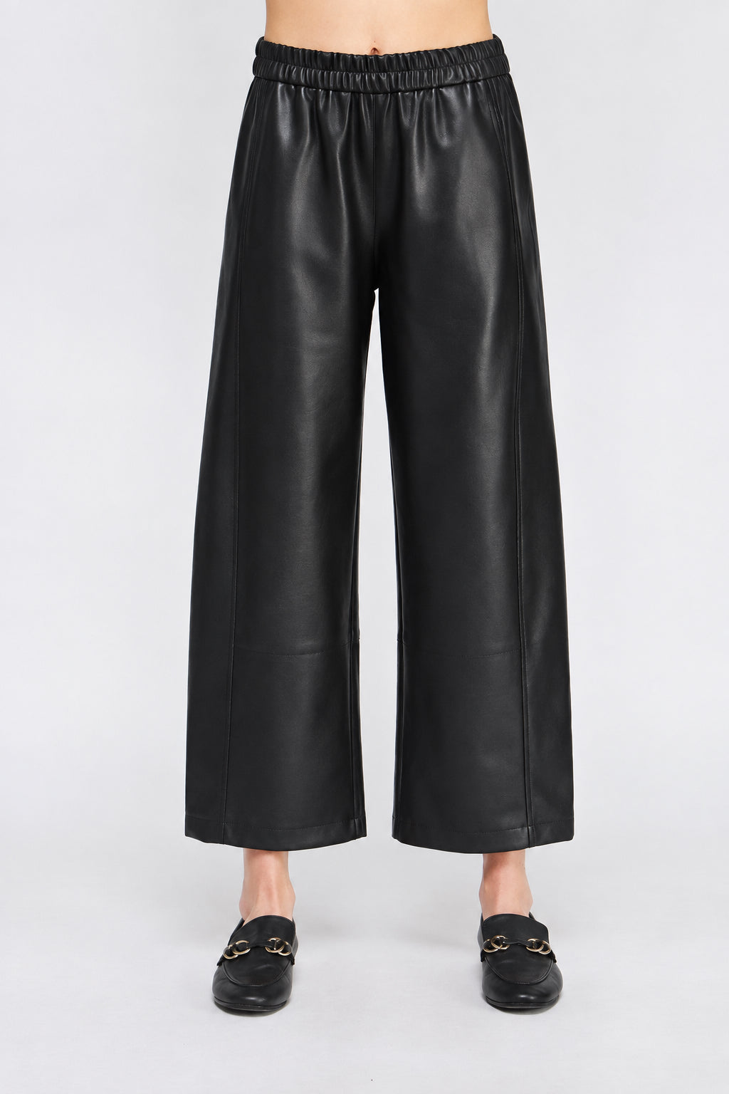 Black wide barrel leg faux leather pants with an elastic waistband, shown on a model wearing black loafers.
