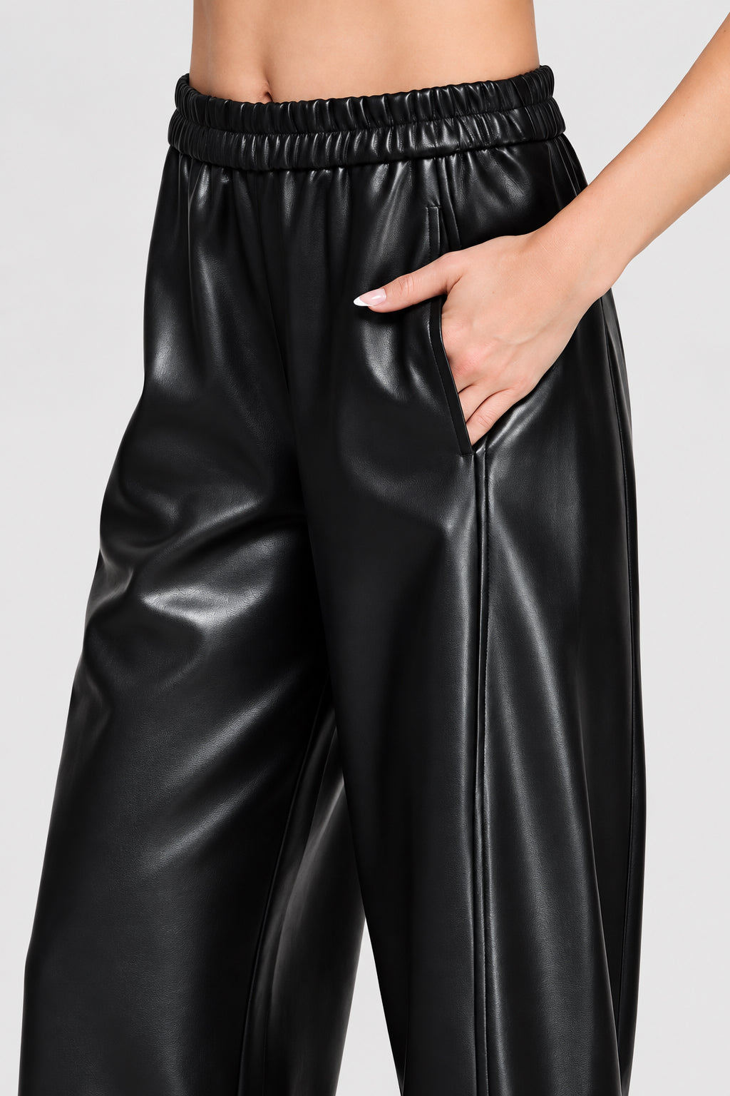 Black wide barrel leg faux leather pants with an elastic waistband and side pockets shown on a model wearing black loafers.