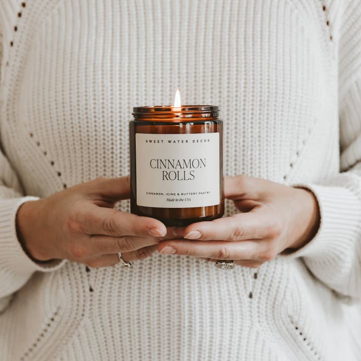 Person holding a 'Cinnamon Rolls' candle with a neutral background