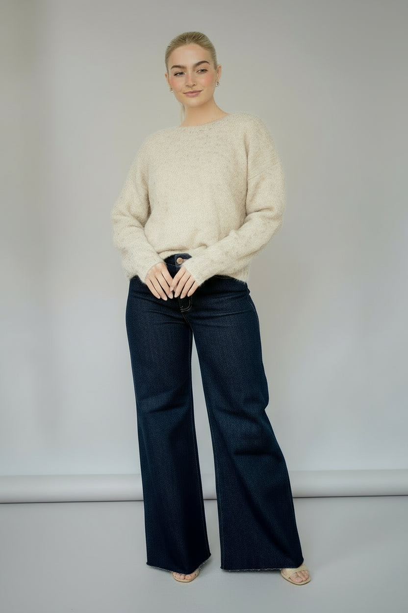 Woman wearing a gold foil speckled ecru knit sweater and blue jeans against a white background