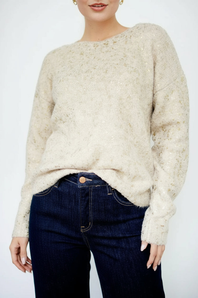 Woman wearing a gold foil speckled ecru knit sweater against a white background