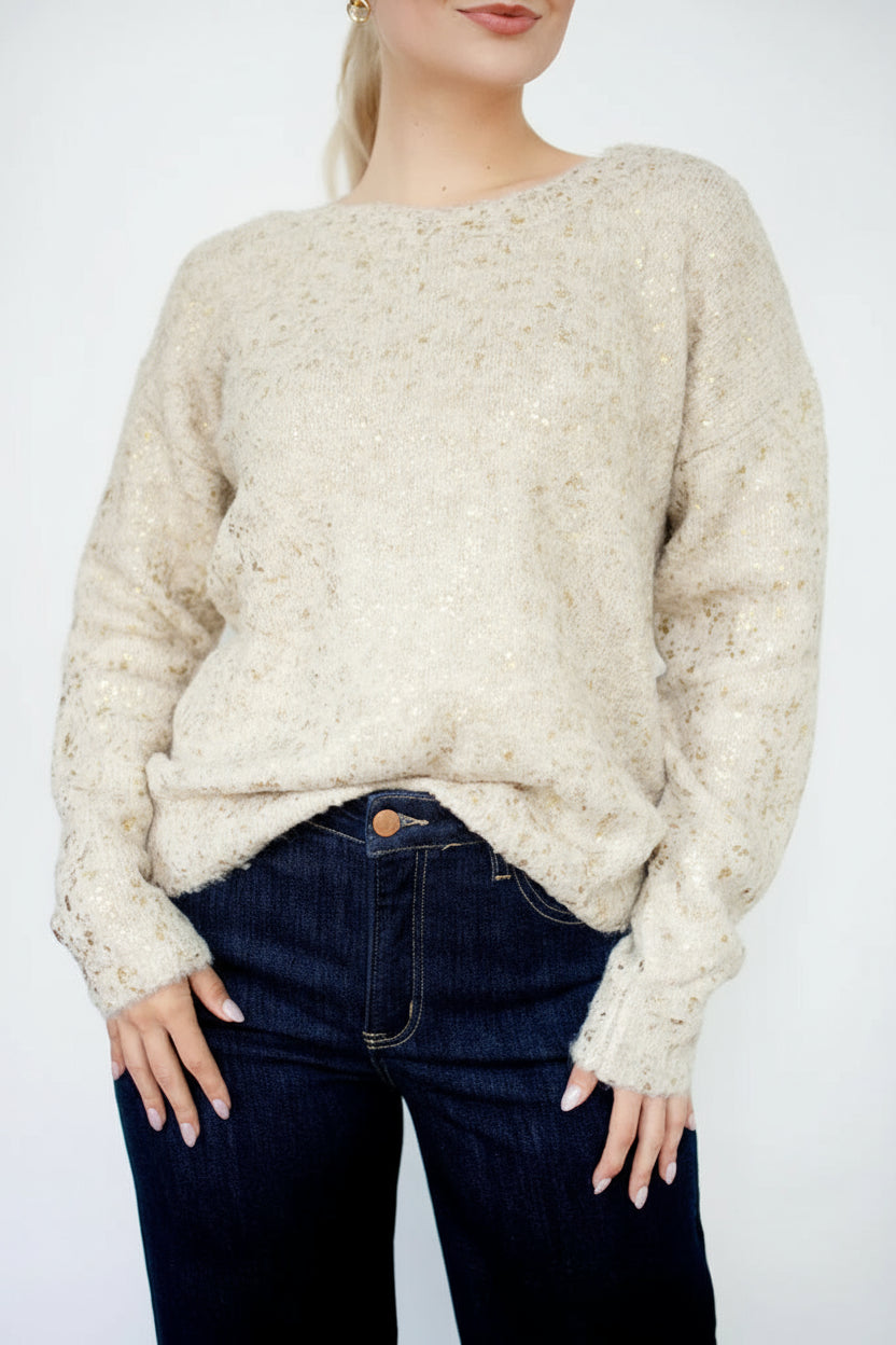 Woman wearing a gold foil speckled ecru knit sweater against a white background