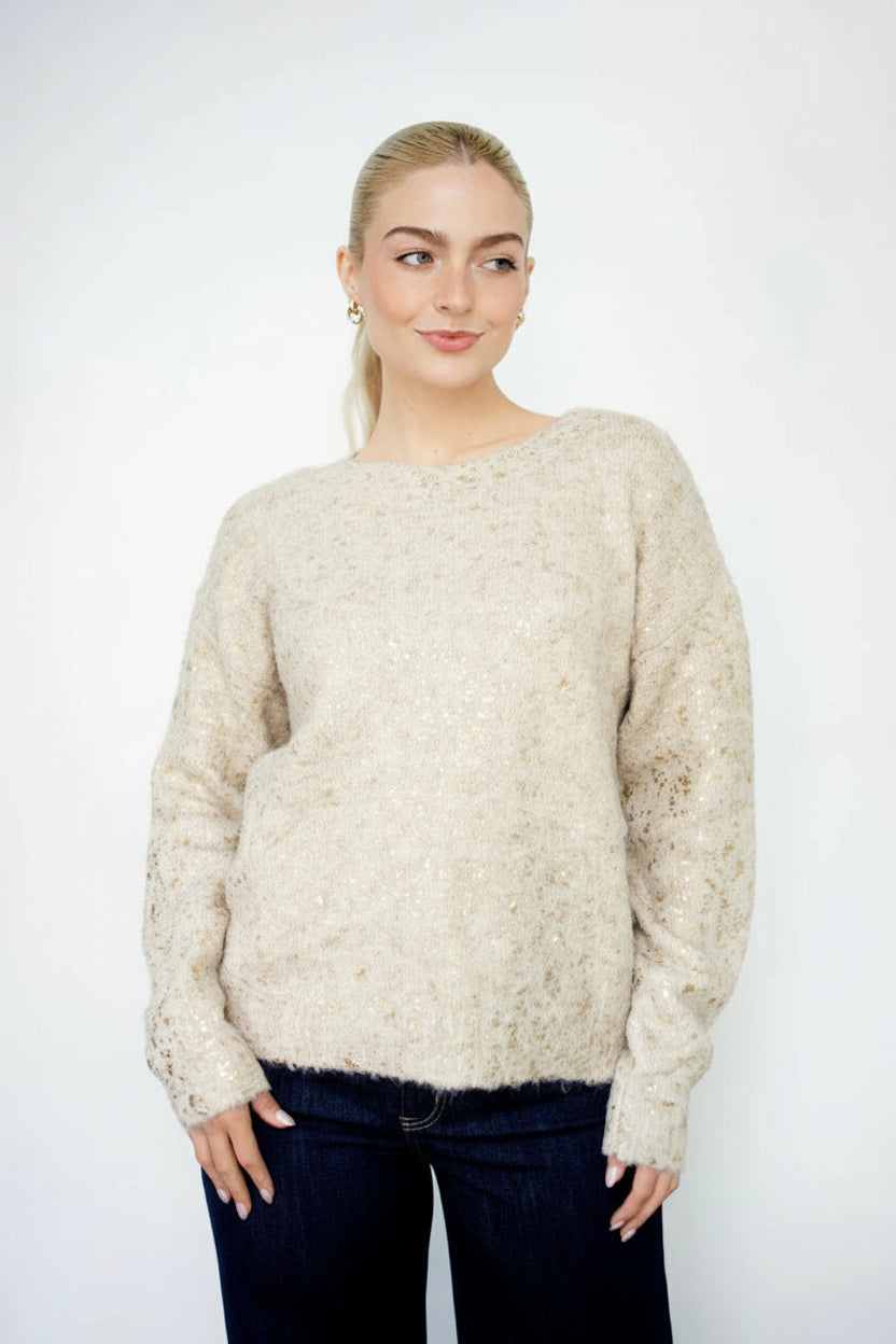 Woman wearing a gold foil speckled ecru knit sweater against a white background