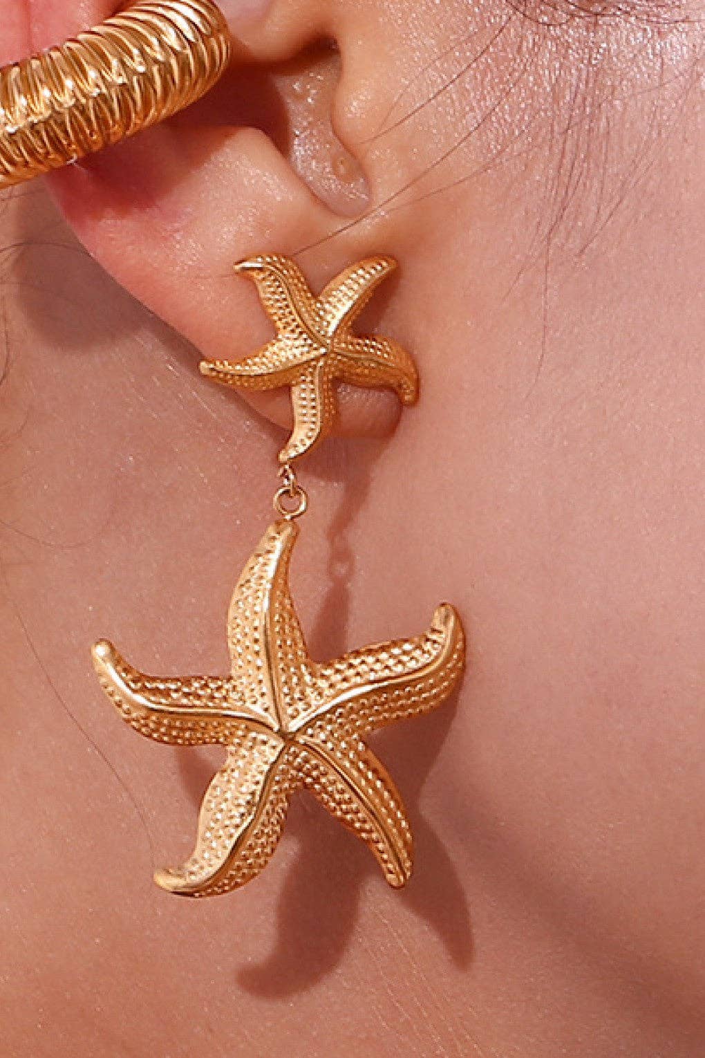 Woman wearing gold starfish dangle earrings