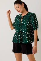 Woman wearing a green polka dot blouse and black shorts on a plain background