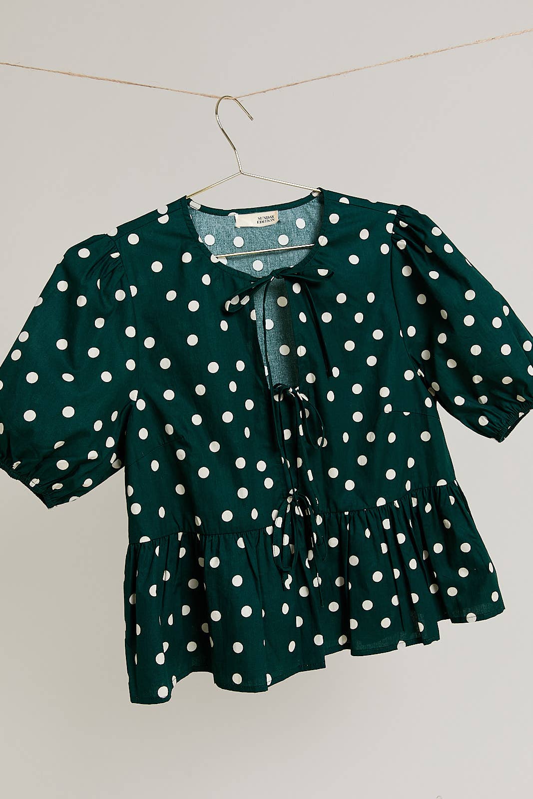 Dark green blouse with cream polka dots on a hanger against a light background