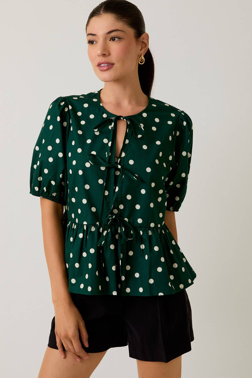 Woman wearing a green polka dot blouse with a plain background