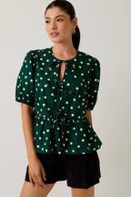 Woman wearing a green polka dot blouse with a plain background