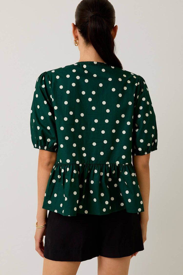 Woman wearing a green polka dot blouse against a plain background