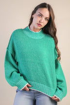 Woman wearing a green mock neck knit sweater with white trim against a beige background